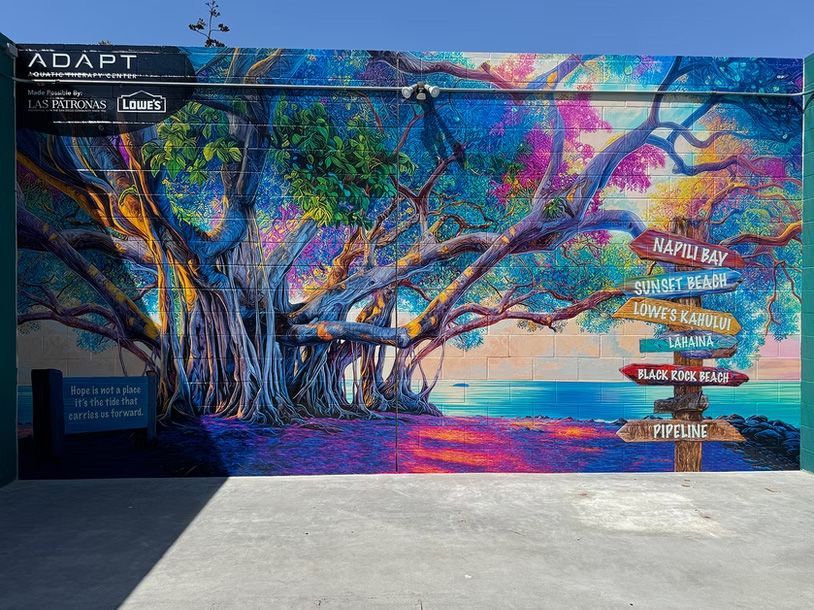 Colorful mural of trees and birds on a building wall with directional signs and a walkway in front