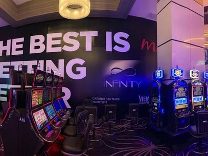 Casino floor with slot machines and a neon wall sign reading “THE BEST IS GETTING… INFINITY”