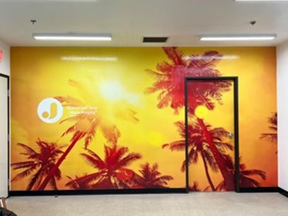 Bright yellow wall mural with palm trees and a pink sunburst in a hallway.