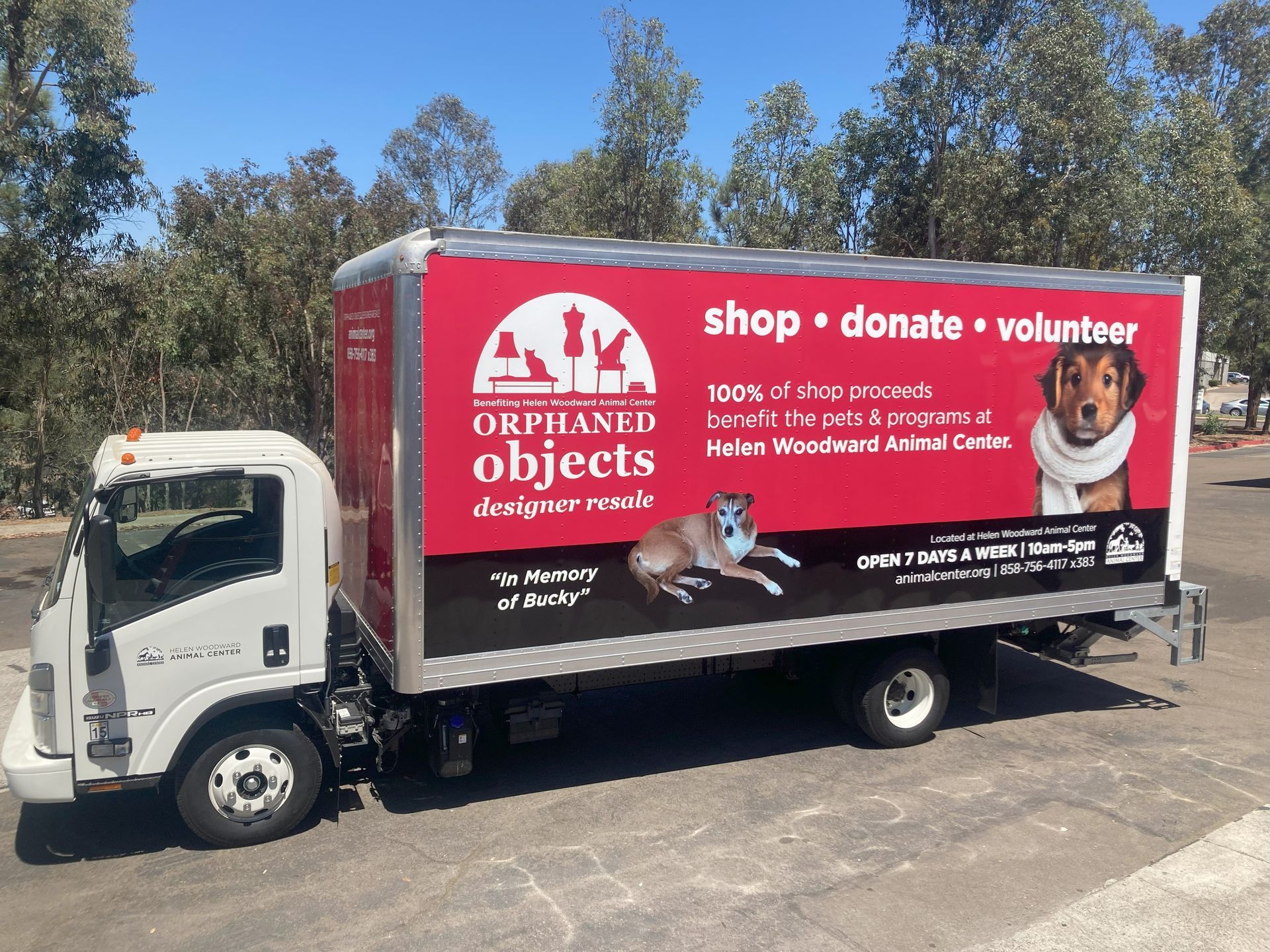 White box truck with a red Orphans’ Objects donation and volunteer ad parked outdoors under blue sky