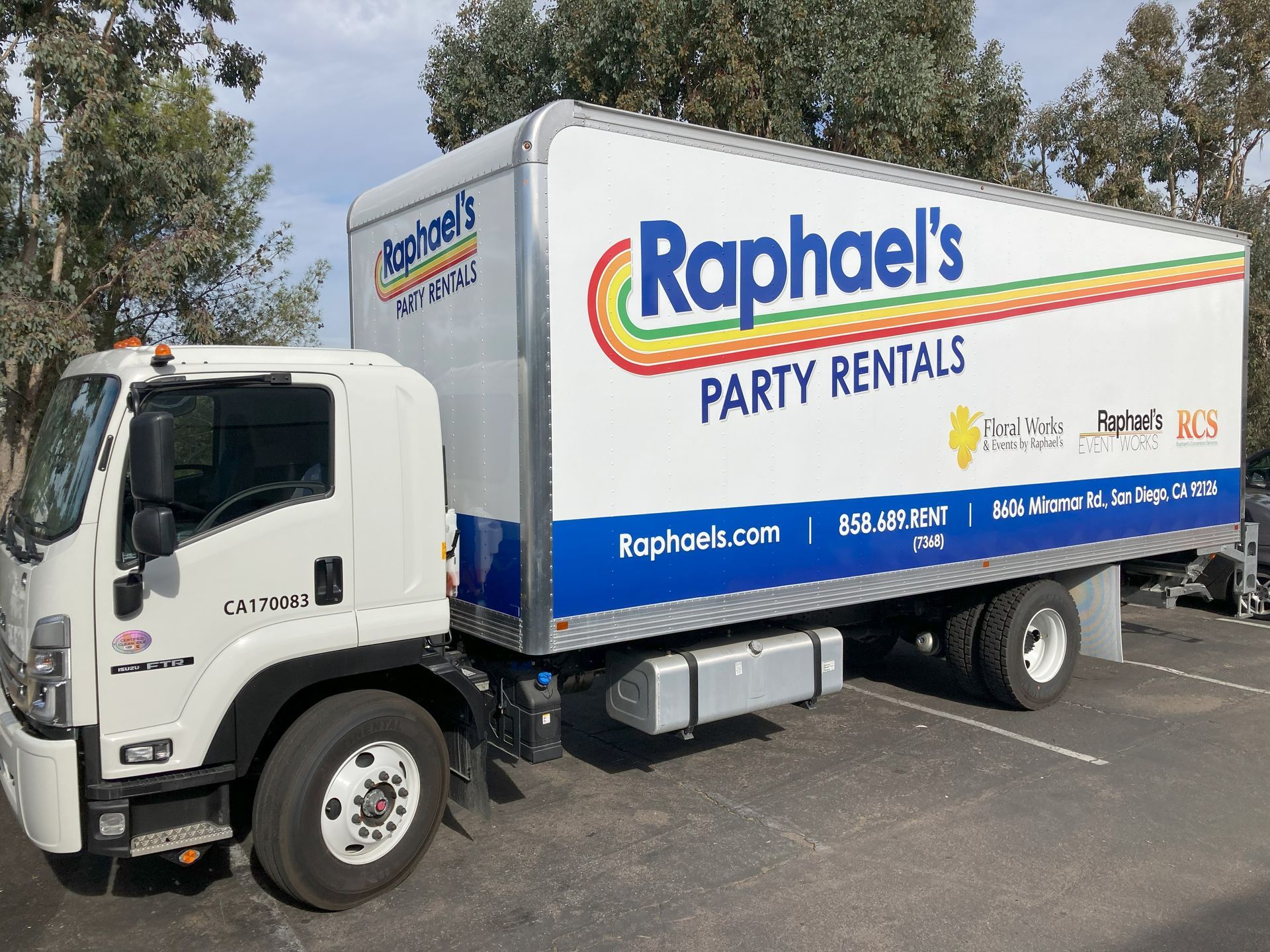 Raphael’s party rental truck parked outdoors, white cab and trailer with blue logo and rainbow stripe