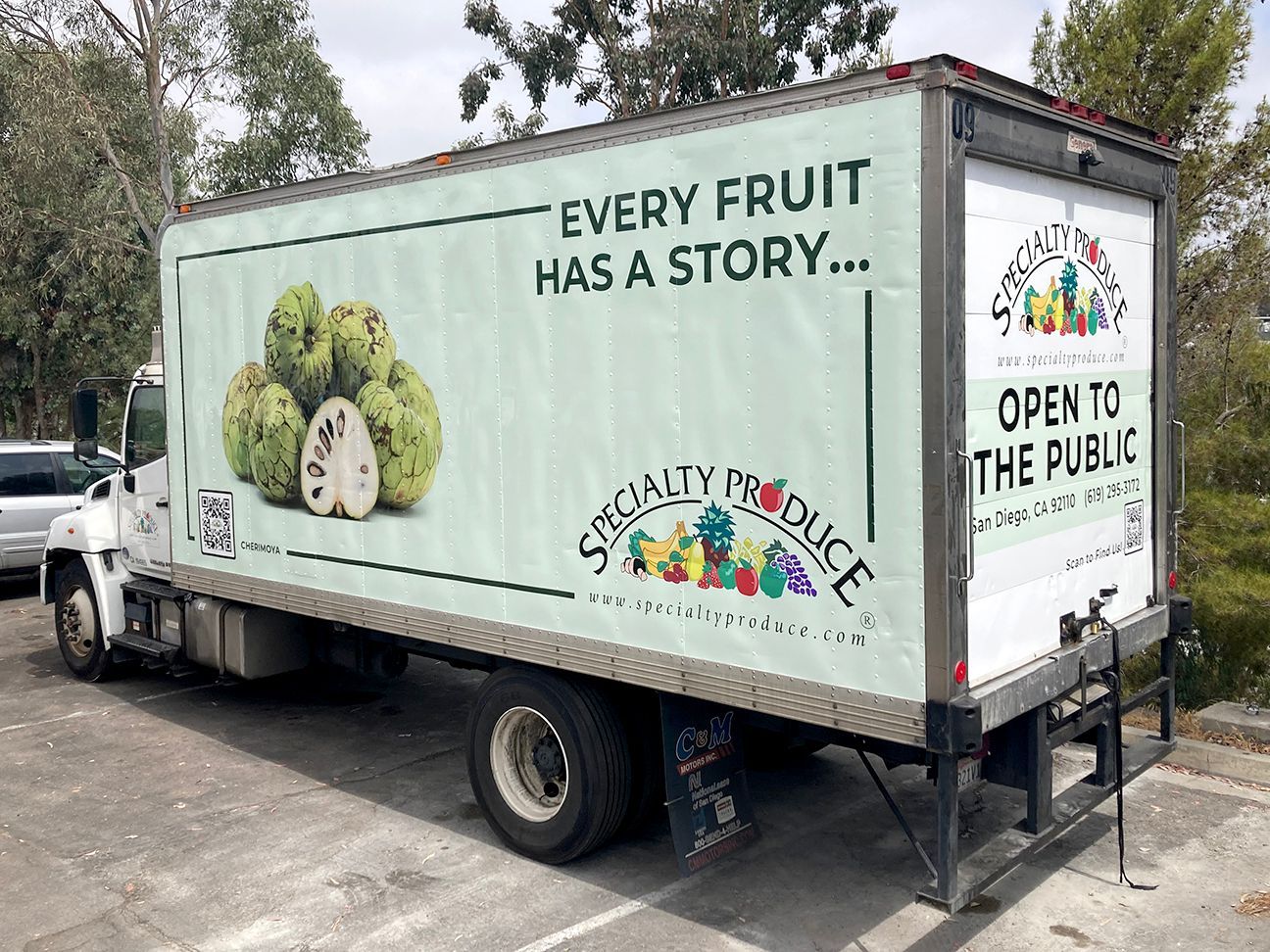 Fruit delivery truck with “Every Fruit Has a Story” and “Open to the Public” text parked outdoors.