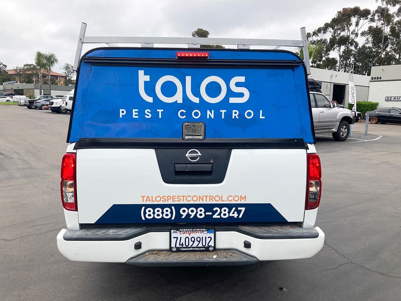 Blue Tanos Pest Control pickup truck parked in a lot, rear view with company logo and phone number.