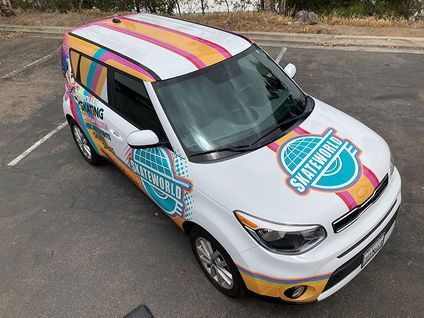 White car with colorful striped roof and bright logo decals parked on pavement