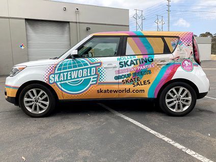 Skateworld-branded white van with colorful skate-themed wrap parked outside a gray building.