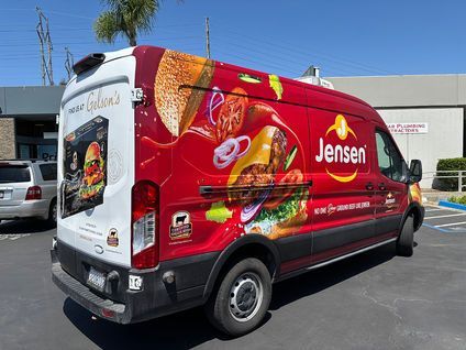 Red Jensen delivery van with food graphics parked in a lot under a blue sky