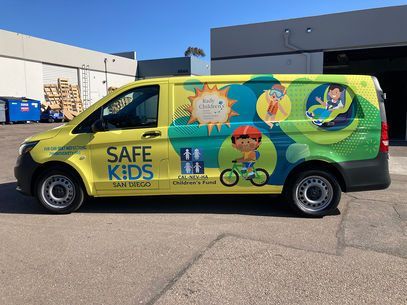 Yellow-and-green Safe Kids van parked outdoors in a lot, with child safety graphics on the side.