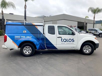 White and blue Talos service truck parked outdoors near palm trees and buildings