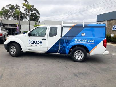 White and blue TALOS service van parked outdoors, side view with company branding and phone number.