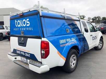Talos Pest Control blue-and-white service truck parked in a lot, rear side view