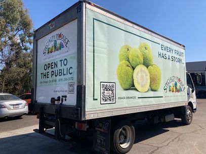 Side of white box truck with produce ad and Open to the Public text parked outdoors