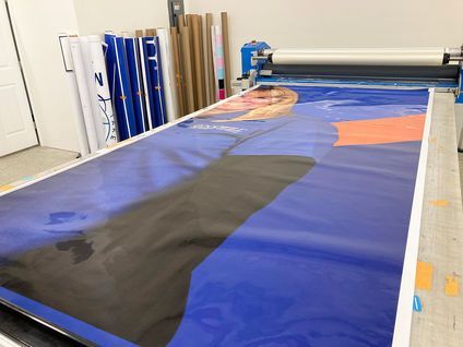 Large-format printer outputting a blue banner with black and orange shapes in a workshop