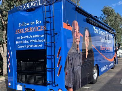 Blue Goodwill bus with Free Services sign and a man standing beside it in a parking lot