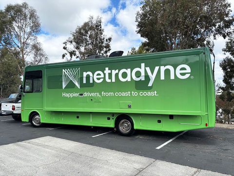 Green Netradyne bus parked in a lot with trees and cloudy sky behind it