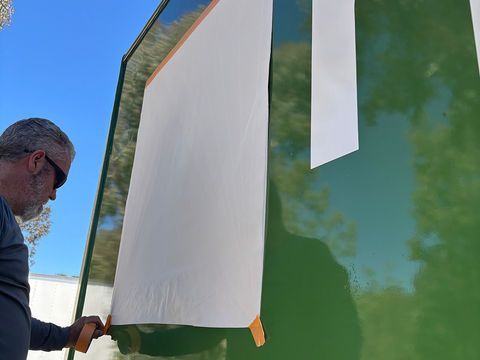 Man hanging a large white banner outdoors against a green wall under a blue sky