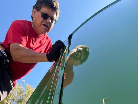 A man in a red shirt is washing a car windshield under a blue sky
