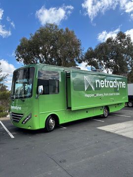 Green Netradyne delivery truck parked outdoors under a blue sky with trees