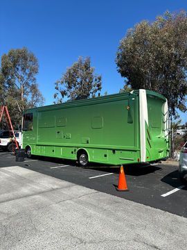 Bright green mobile trailer parked in a lot with orange cones and trees under a blue sky
