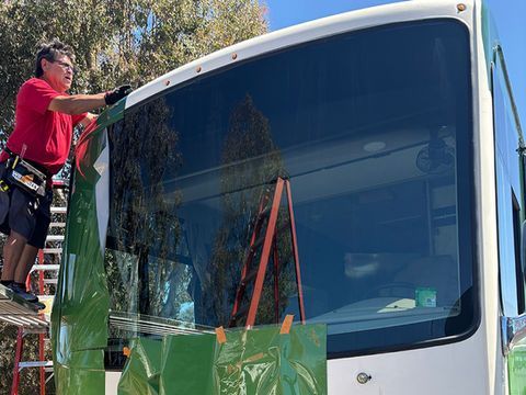 Worker on a ladder cleaning the windshield of a white bus outdoors