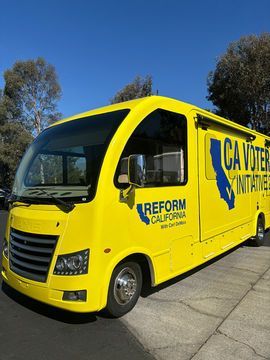Bright yellow Reform California campaign bus parked outdoors on a sunny street