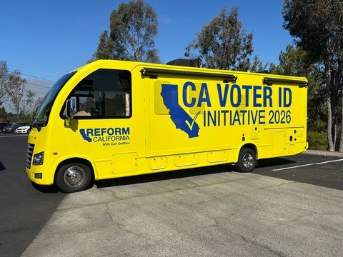 Yellow bus with CA VOTER ID INITIATIVE 2026 parked outdoors under trees