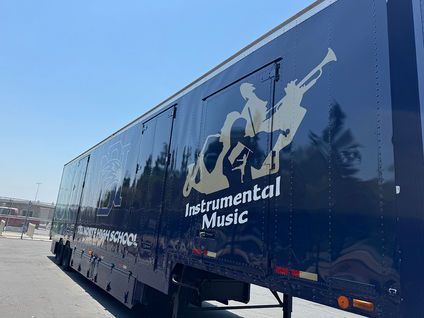 Blue trailer with Instrumental Music logo and figures on the side, parked outdoors.