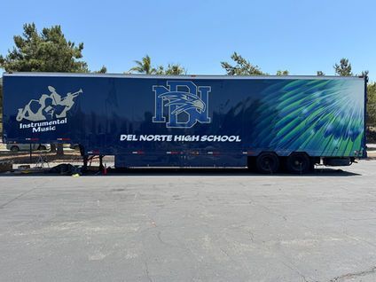 Blue Del Norte High School trailer parked in a lot under a clear sky, with school logos on the side
