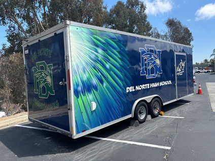 Blue DEL Norte High School trailer with sports graphics parked in a lot on a sunny day