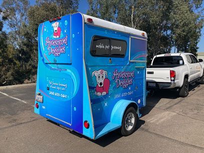 Blue food trailer with cartoon logo parked on a street beside a white pickup truck.