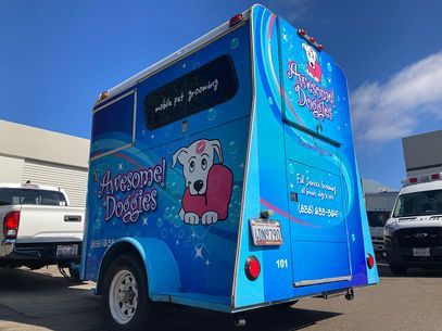Blue ice cream truck with a cartoon pig logo parked outdoors under a bright sky