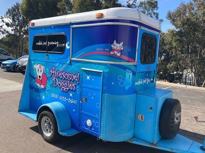 Blue Frozen Dog pet grooming trailer parked outdoors, with cartoon graphics and a small side door