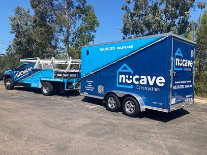 Blue Nucave Construction vehicles parked outdoors on a sunny day, a blue truck and trailer with a logo.
