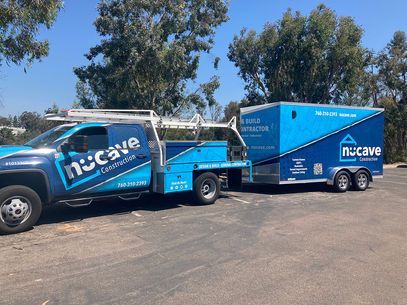 Blue Nucave Construction service truck towing a branded trailer parked outdoors on pavement under trees