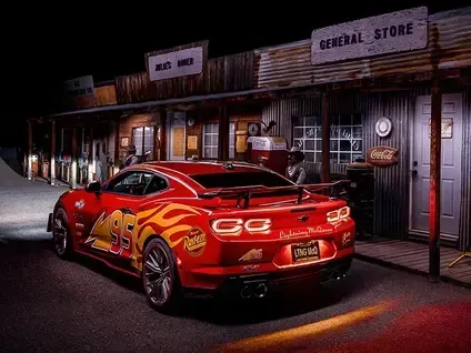 Red sports car parked on a dimly lit street in front of a general store at night
