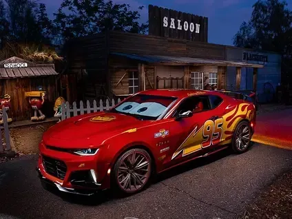 Red sports car with racing decals parked outside a rustic saloon at dusk