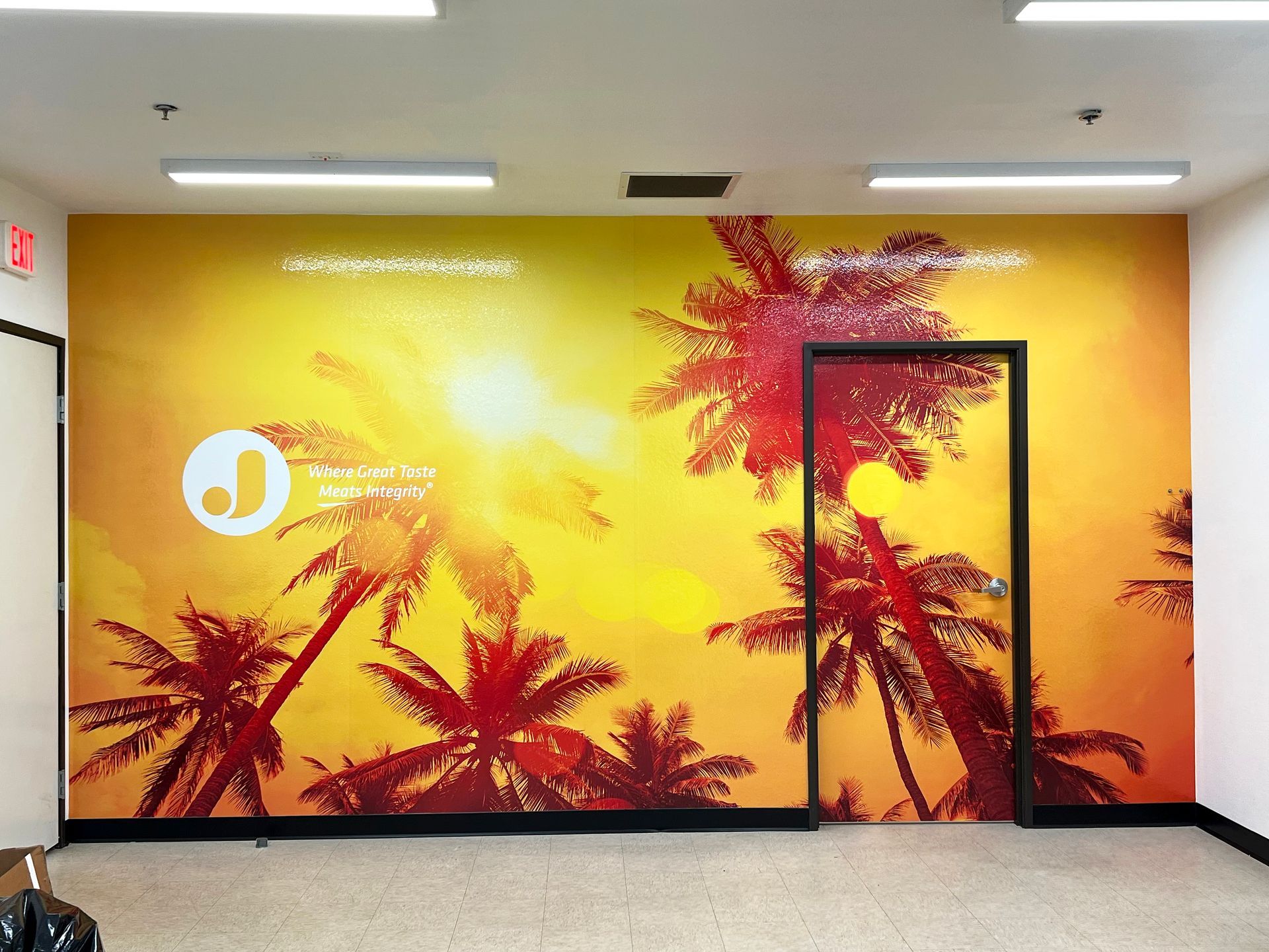 Bright tropical mural with palm trees and a sunburst in a hallway, featuring an orange-yellow wall and door