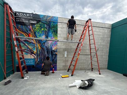 People painting a colorful mural on a concrete wall with ladders in a courtyard