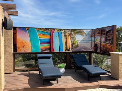 Outdoor lounge with two black chaise lounges beneath a colorful surfboard-style mural.