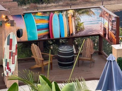 Rooftop deck with surfboards, colorful wall art, barrels, and seating around a small outdoor table
