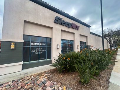 Sleeper furniture store exterior with glass windows, gray facade, and desert landscaping under cloudy sky