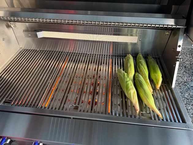 Corn on the cob grilling on a stainless steel grill.