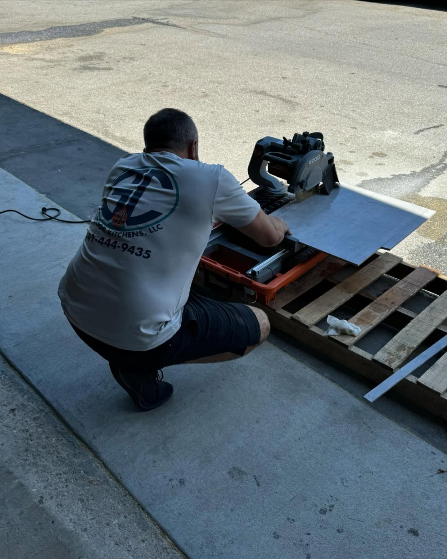 Person using a saw to cut a metal sheet on a wooden pallet outdoors.