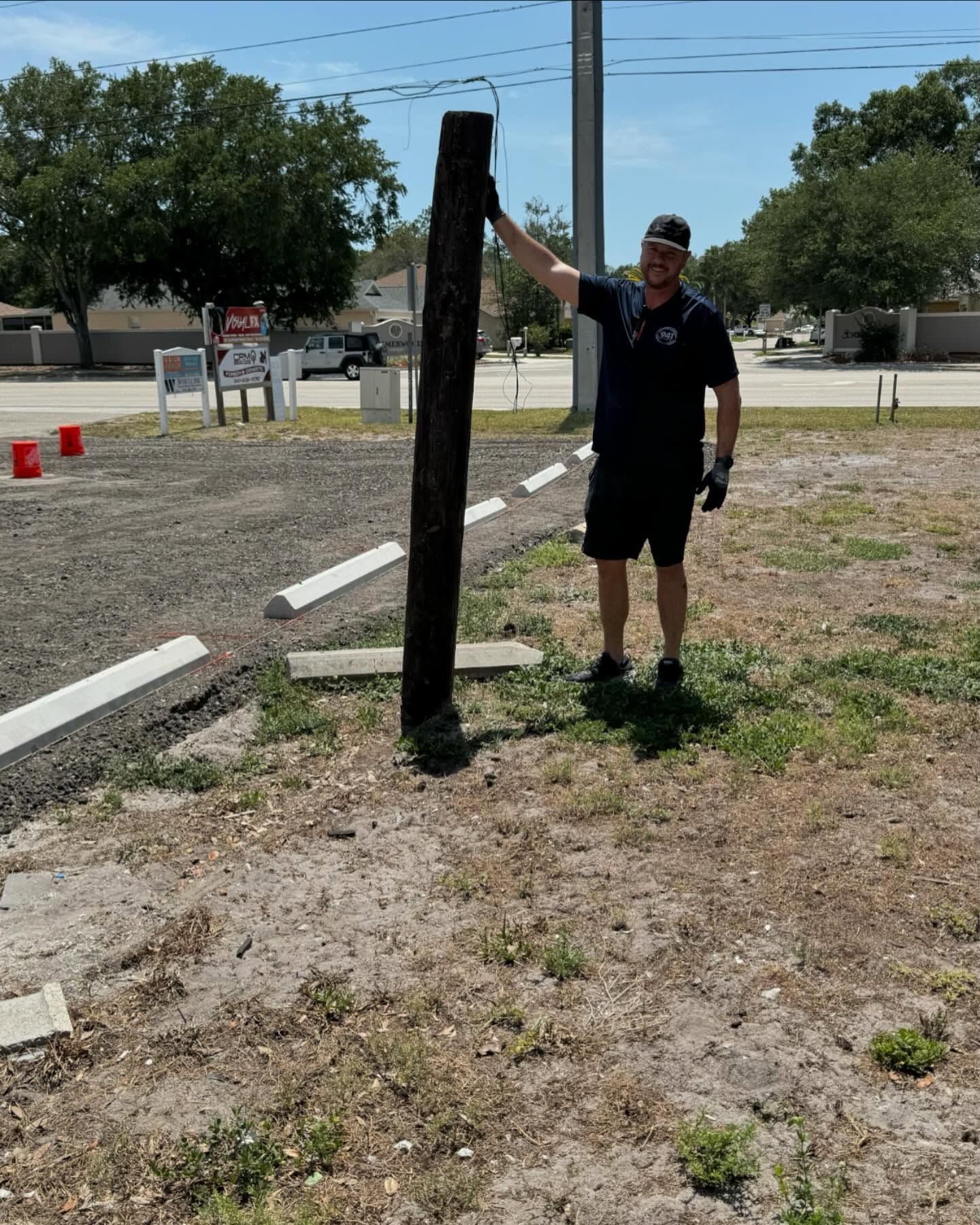 Man holding up a dark wooden pole in a grassy parking area.