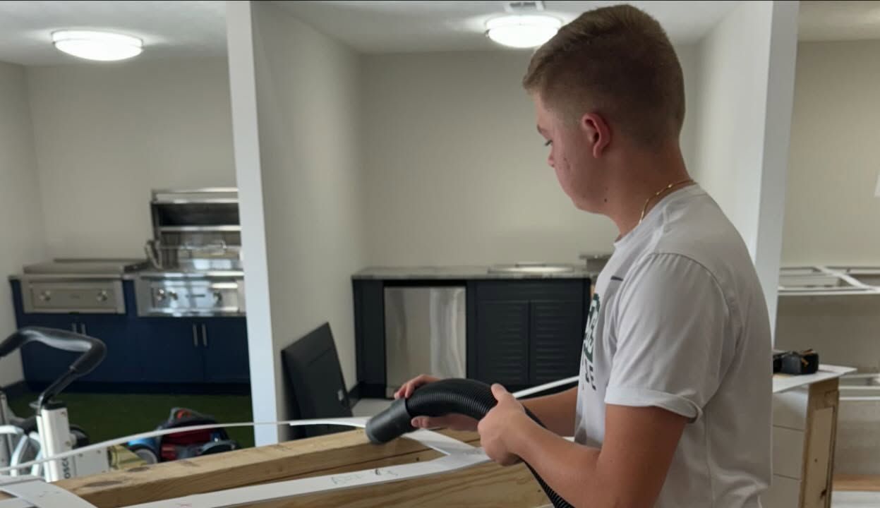 Person holding a black hose inside a room with a kitchen area.