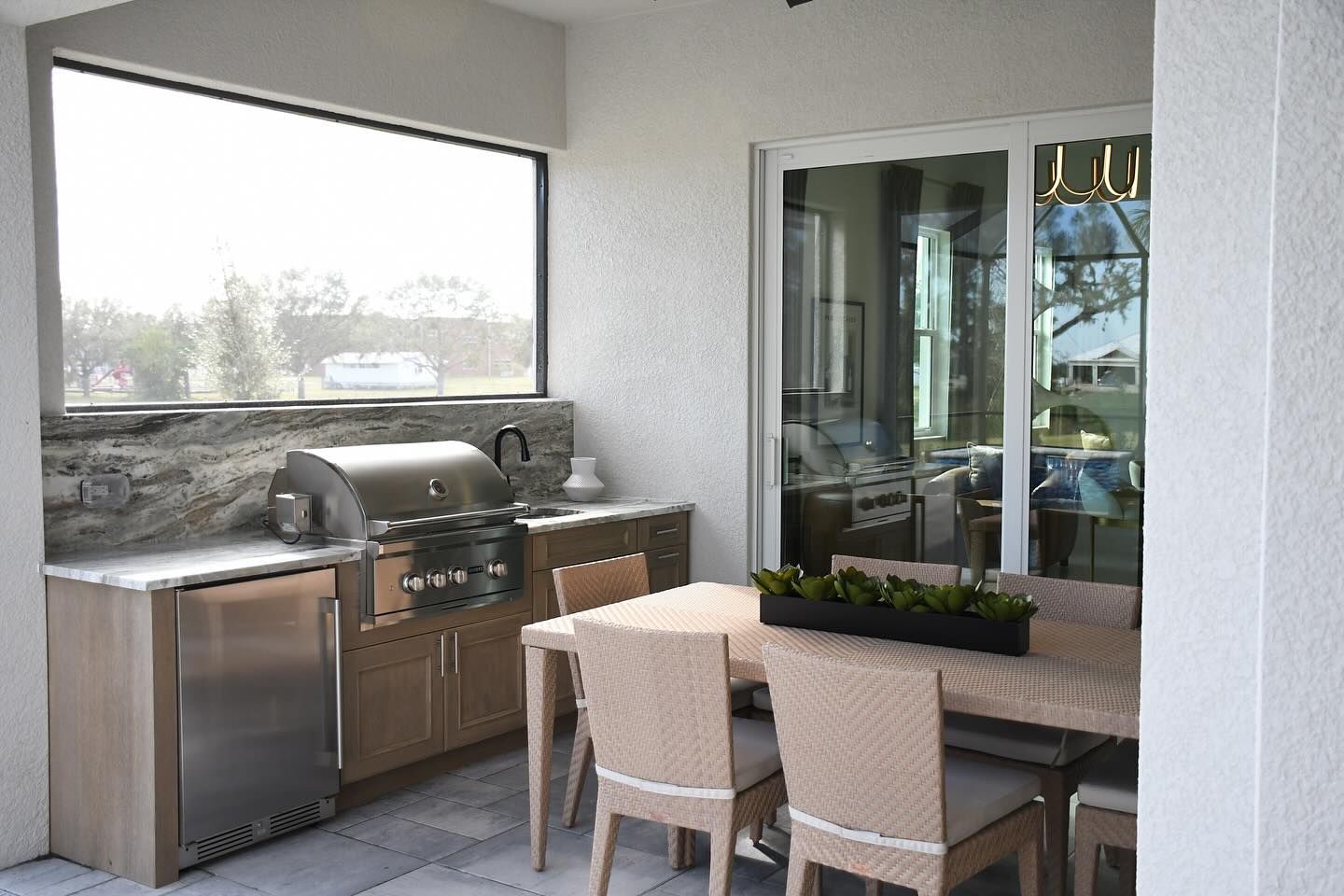 Outdoor kitchen with grill, fridge, cabinets, table, and chairs.