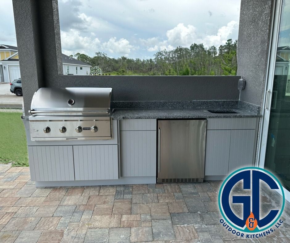 Outdoor kitchen with stainless steel grill, cabinets, and refrigerator on a patio with a view.