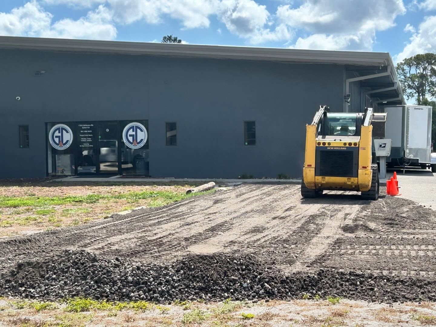 A yellow skid steer leveling gravel in front of a gray building with 
