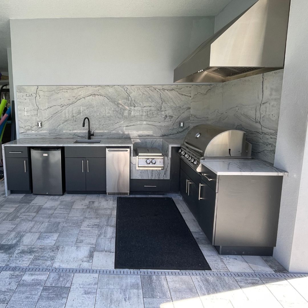 Outdoor kitchen with gray cabinets, stainless steel appliances, and marble backsplash.