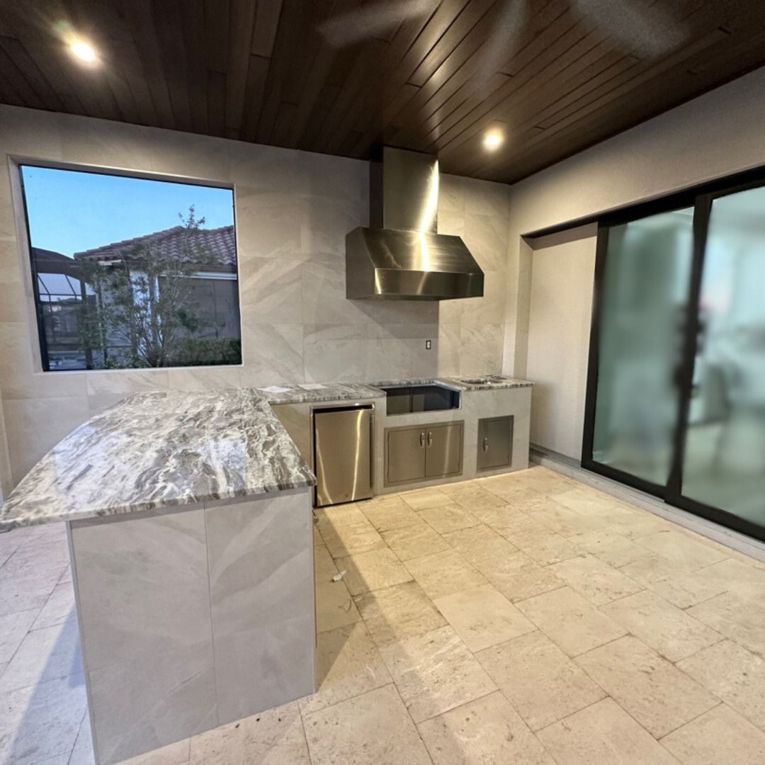 Outdoor kitchen with granite countertop island, stainless steel appliances, and large window.