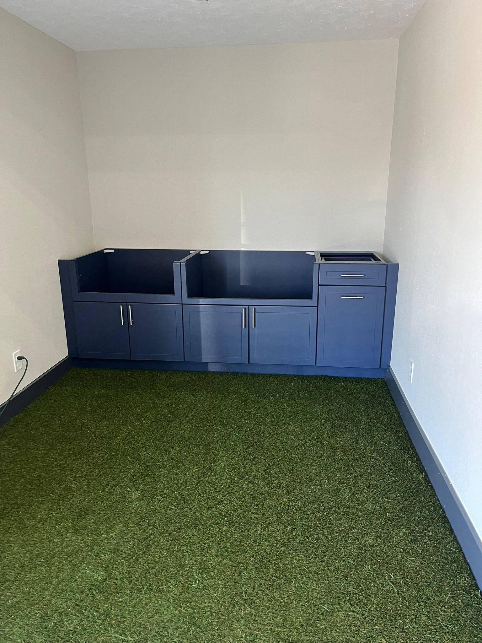 A dark blue built-in storage unit against a white wall in a room with green turf flooring.